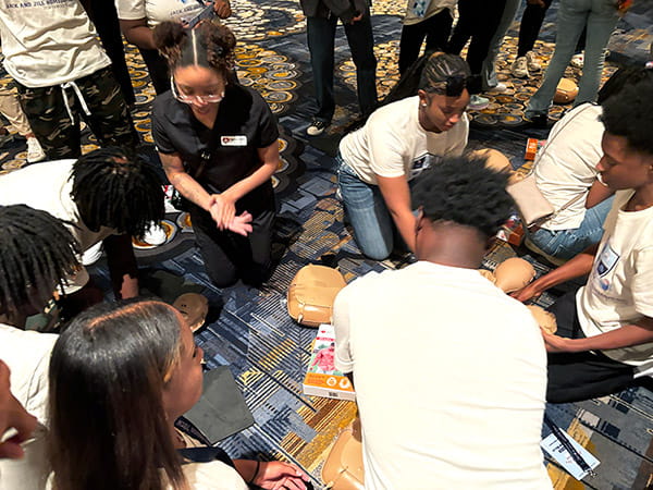 A group of young people are on the ground practicing chest compressions on CPR manikins.