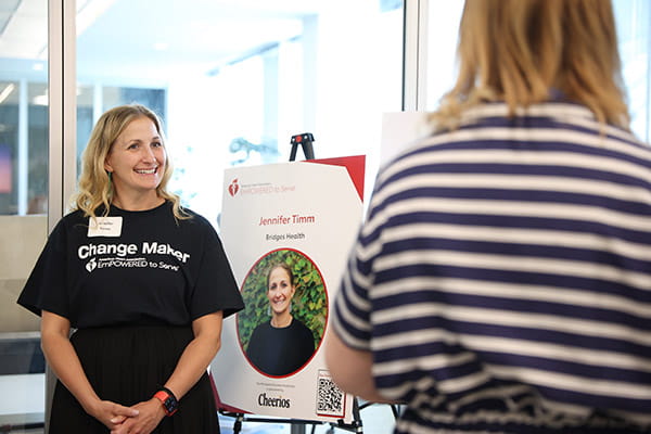 Jennifer Timm is standing in front of a presentation board as she speaks to someone about her program, Bridges Health, at the ETS Minnesota Business Accelerator finale