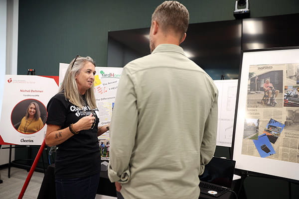 Nichol Dehmer is talking with an event guest at her table at the ETS Minnesota Business Accelerator finale