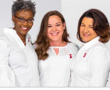 Three diverse women wearing white are smiling.