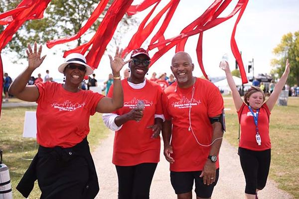 A group of smiling people wearing red is walking down a sidewalk and cheering. A group of smiling people wearing red is walking down a sidewalk and cheering.